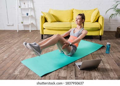Positive sportswoman working out near laptop and bottle of water on floor - Shutterstock ID 1837950637