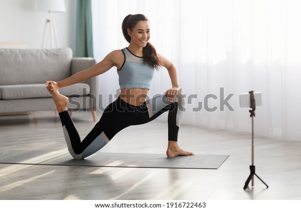 Positive\
sporty lady stretching in front of smartphone at home, copy space.\
Beautiful young woman fitness blogger shooting video for her\
followers or having personal training\
online