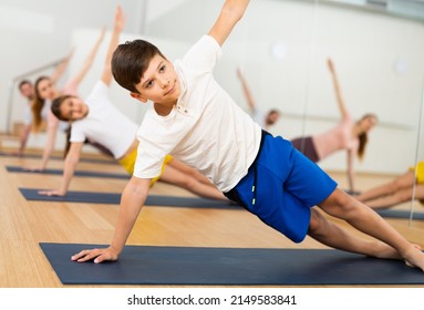 Positive Sporty Teen Boy Doing Yoga With Sister And Parents In Fitness Studio, Standing In Side Plank Or Vasisthasana Pose..