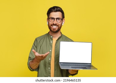 Positive Stylish Man Showing Brand New Laptop With Blank White Screen Over Yellow Studio Background, Recommending Website Or Demonstrating Your Ad, Copy Space, Mockup