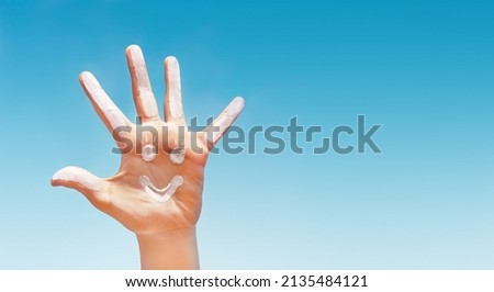 Positive symbol drawing by sunscreen (sun cream, suntan lotion) on caucasian open hand on blue sky background. Concept of protection (safety) from sun, skin care, happy summer vacation. Copy space. 
