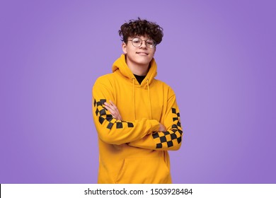 Positive teen boy in yellow hoodie crossing arms and looking at camera against bright violet background - Shutterstock ID 1503928484