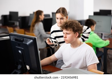 Positive Teen Girl Student Talking To Concentrated Teenager Studying In College Library Computer Lab..