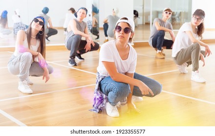 Positive teen girls and boys hip hop dancers squatting during group dance workout