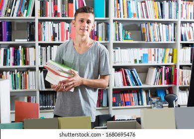 Positive Teenage Boy Holding Book Pile In Hands In Book Shop
