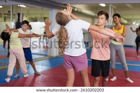Positive teenager kids in pair exercising self-defense movements during group class
