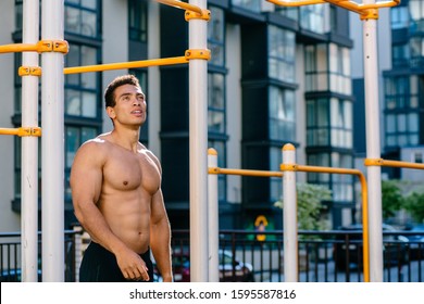 Positive topless muscular athlete under sports bar after pulling up on sportsground during workout.Naked torso man looking away, relaxing after exercises. Sport, lifestyle and people concept.