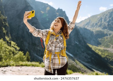 Positive tourist woman taking picture outdoors for memories, making selfie with valley mountains view, sharing travel adventure journey. Lifestyle, travel, tourism, active life. - Powered by Shutterstock