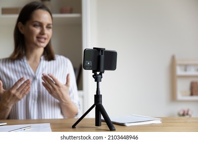 Positive Trendy Blogger Woman Speaking At Smartphone Webcam On Tripod, Recording Post For Vlog. Online Teacher, Coach Working, Giving Webinar At Home. Presenter Taking Video On Cellphone. Close Up