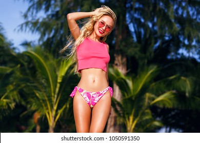 Positive Vivid Portrait Of Pretty Happy Blonde Woman, With Perfect Healthy Slim Body Having Fun On The Tropical Beach, Sunny Hot Weather, Palm Trees Around, Bikini Body , Pink Beachwear.