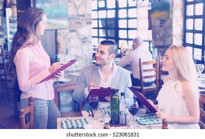 Positive waitress taking table order and smiling at tavern