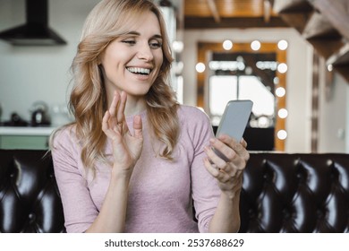 Positive woman Caucasian lady european female using mobile phone for watching video having video call sitting in minimalist living room home interior. Chat in social networks, app for communication - Powered by Shutterstock