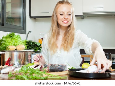 Positive Woman Cooking Fish In Flour At Kitchen Table In Home