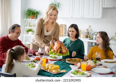 Positive Woman Holding Turkey Near Multicultural Family And Food At Home