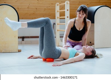 Positive Woman Instructor Helping Client Doing Self-massage Technique Applying Franklin Ball For Pelvis Or Hip On Sacroiliac Joint Pain Area Pain Relief, Working Out Lying On Floor In Pilates Studio.