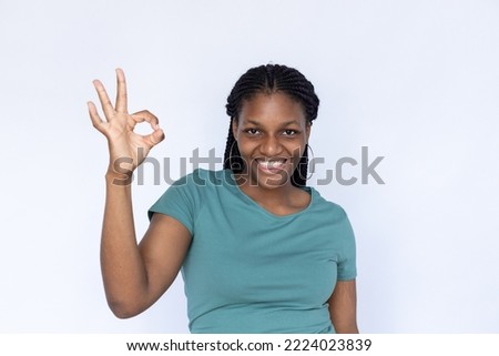Positive woman making okay gesture. Young female model in turquoise T-shirt showing okay sign smiling looking at camera. Portrait, studio shot, advertising concept