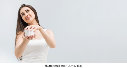 Positive woman opens jar of nourishing cream on light background in studio - Shutterstock ID 2174874885