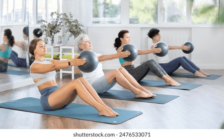 Positive woman performing set of exercises with pilates balls during group class with of different ages in fitness studio - Powered by Shutterstock