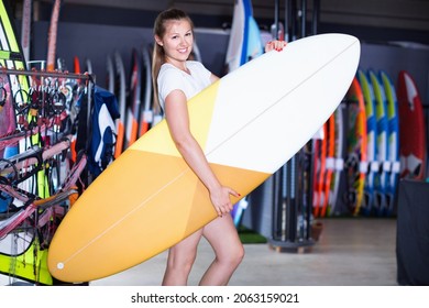 Positive woman is posing with surfboard in store on the beach. - Shutterstock ID 2063159021