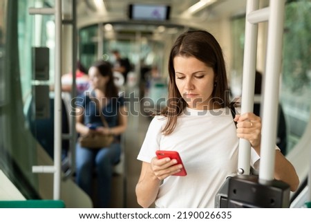 Positive woman reading from mobile phone screen in the cabin of bus or tram. High quality photo