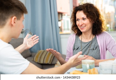 Positive Woman With Teen Son Enjoying Time At Home, Having Friendly Conversation