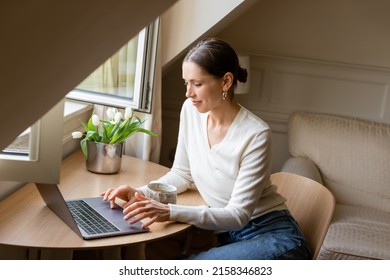 positive woman typing on laptop near window, clay cup and fresh tulips