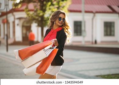 Positive Woman Walking At Street After Shopping With Many Paper Bags.