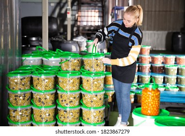 Positive woman working at the warehouse, stacking plastic containers with the selected olives. High quality photo