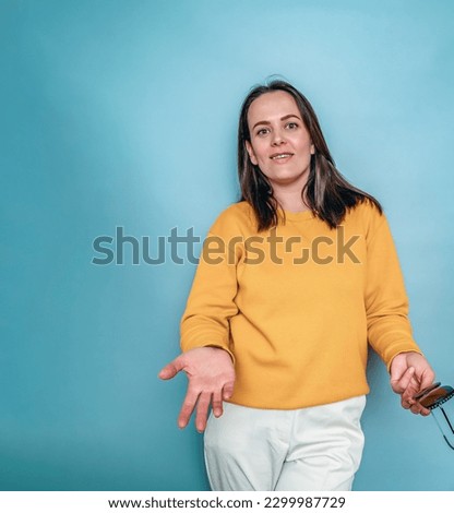 Positive woman in yellow spread her arms to sides. Blue background. Interrogative emotion.