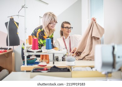 Positive Working Environment As Two Female Tailors Check The Quality Of Their Work In A Small Workshop.