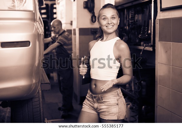 Positive\
working woman holding cardboard in car\
workshop