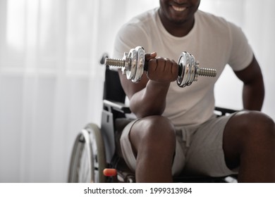Positive workout, training in clinic, strength exercises, recovery at home. Cheerful adult african american guy in wheelchair lift up dumbbell in living room interior, cropped, copy space, close up