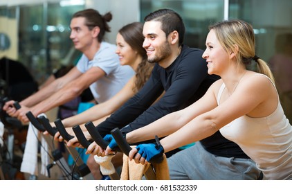 Positive young adults working out of cycling in modern fitness club . Selective focus
