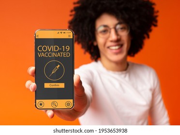Positive young African American guy holding cellphone with immune passport for covid-19, showing proof that he has been vaccinated. Digital Green Certificate. Selective focus, blurred background