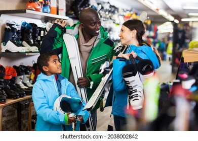 Positive Young African Man And European Woman With Preteen Son Choosing Together Ski Boots For Skiing In Store Of Sports Gear