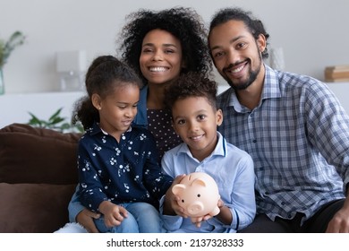 Positive Young African Parents And Little Kids Showing Piggybank With Cash, Saving Money In Moneybox, Making Donation Fund, Financial Reserve For Crisis. Happy Family Bank Customers Concept