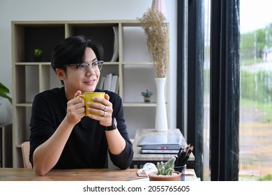 Positive Young Asian Man Holding Coffee Cup And Looking Out Of Window.