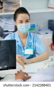 Positive Young Asian Medical Nurse Talking To Patient At Clinic Reception