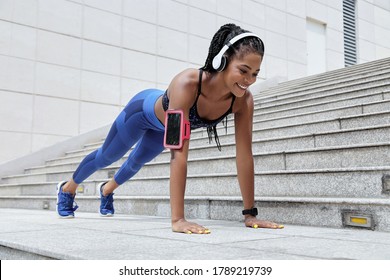 Positive young Black woman listening to music in headphones and doing push-up exercise - Powered by Shutterstock