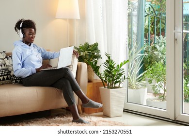 Positive Young Black Woman Wearing Headphones When Editing Video For Her Blog On Laptop