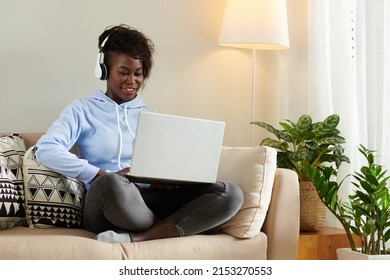 Positive Young Black Woman Wearing Headphones When Playing Game On Laptop At Home