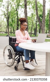 Positive Young Black Woman In Wheelchair Using Laptop In Outdoor Cafe At Spring Park, Working On Online Business Project, Attending Meeting Remotely, Having Educational Webinar, Copy Space
