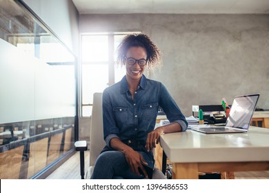 Positive junge Geschäftsfrau sitzt am Büroschreibtisch. Junge afrikanische Frau bei der Arbeit.