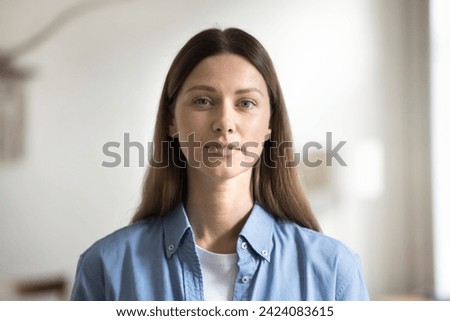 Positive young Caucasian woman with natural makeup, long brown hair in casual shirt looking at camera, posing indoors. Adult 30s female model head shot portrait, video call screen view