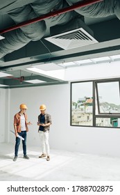 Positive young constructin engineers standing in empty room after checking building acceptance readiness