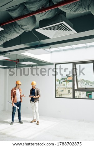 Positive young constructin engineers standing in empty room after checking building acceptance readiness