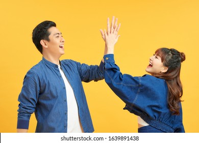 Positive Young Couple Give High Five, Agree To Work As Team, Stand Sideways, Isolated On Yellow Wall. Male Student With Notepad Touches Palm Of Girlfriend, Have Agreement.