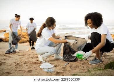 Positive young different people volunteers in gloves with garbage bags clean up trash on sea beach, outdoor. Ocean pollution and environment conservation, protecting planet, Earth day - Powered by Shutterstock