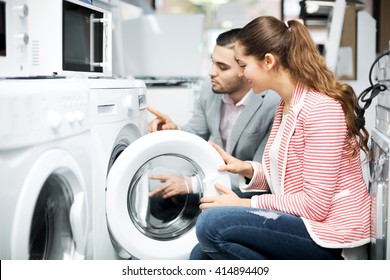 Positive Young Family Couple Buying New Clothes Washer In Supermarket. Focus On The Woman