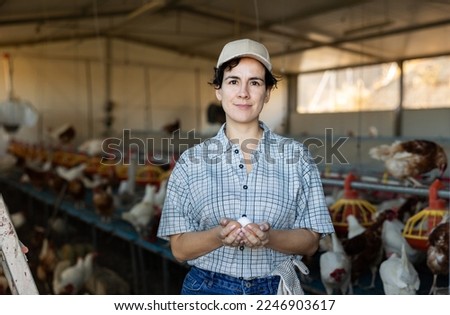 Positive young female farmer working in henhouse, collecting eggs